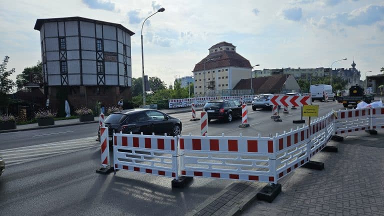 Ulica Limanowskiego w Olsztynie z zamkniętym pasem ruchu i barierami, w tle widoczny wiadukt i budynki.