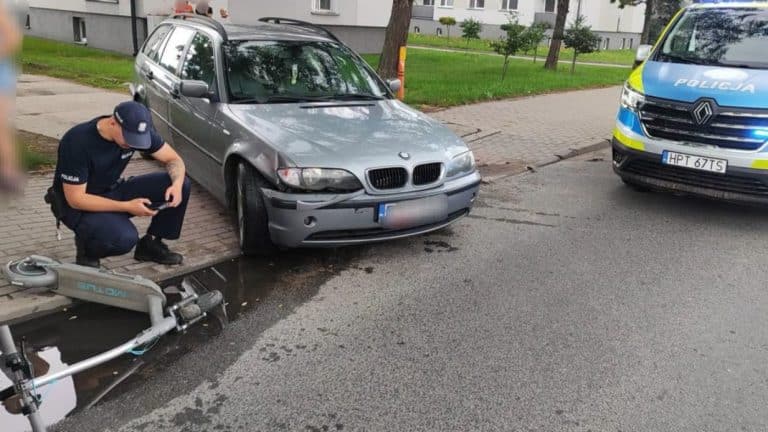 Uszkodzony samochód BMW i policyjny radiowóz na ulicy po wypadku z hulajnogą elektryczną, na miejscu policja.