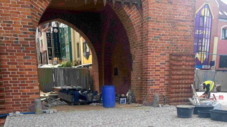 Prace budowlane na placu przed Wysoką Bramą w centrum Olsztyna, widoczny robotnik i materiały budowlane.