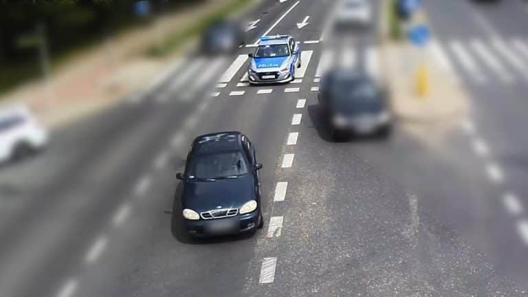 Policja ściga samochód na ulicy w Olsztynie, w tle inne pojazdy i oznakowany radiowóz.
