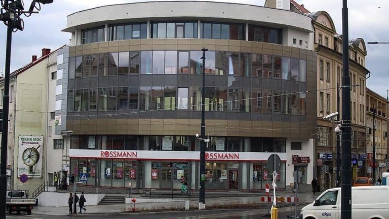 Widok na nowoczesny budynek z dużymi oknami i sklepem Rossmann na parterze, w centrum miasta.