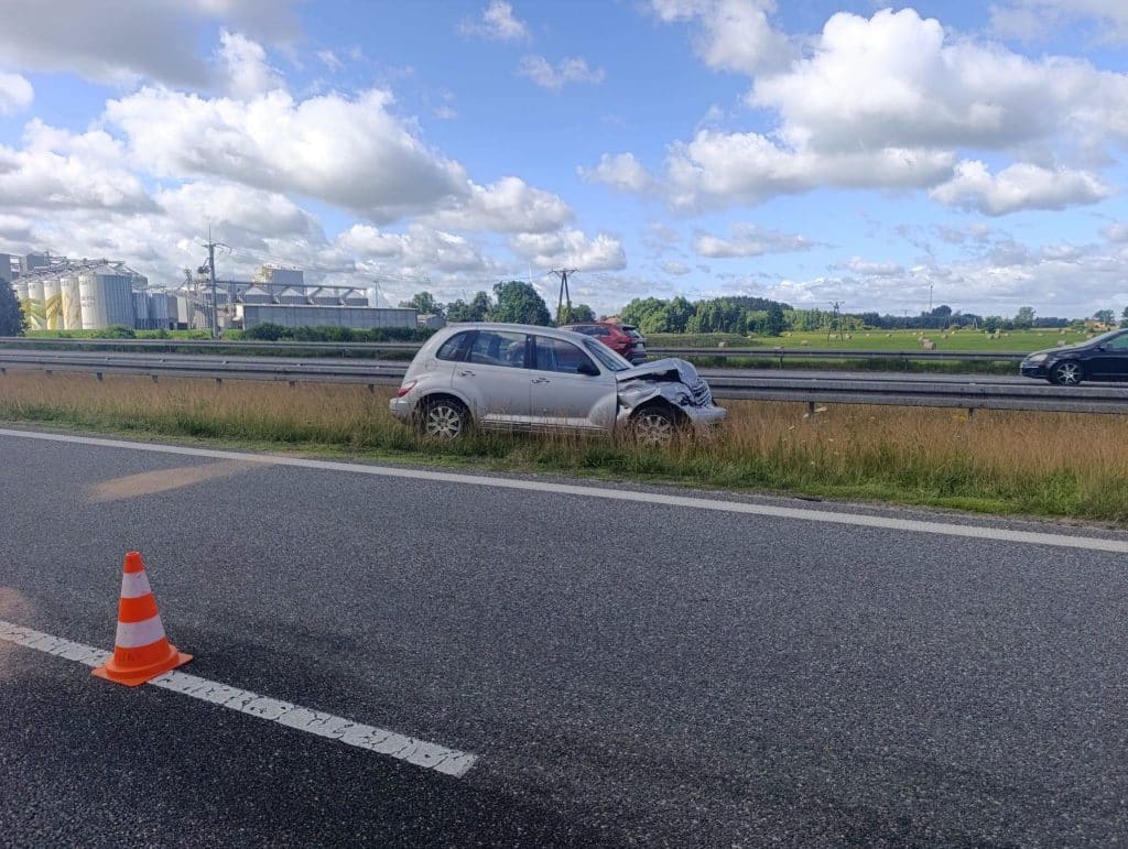 Uszkodzony samochód na poboczu drogi S7 po kolizji z łabędziem, w tle inne pojazdy i krajobraz wiejski.