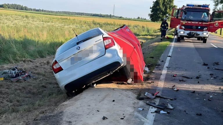 Rozbity samochód osobowy na poboczu po wypadku na drodze krajowej, widoczne służby ratunkowe i rozbity sprzęt ratunkowy.