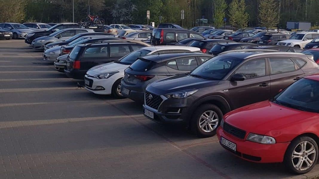 Parking lot pełen różnych samochodów, w tle drzewa i budynki.