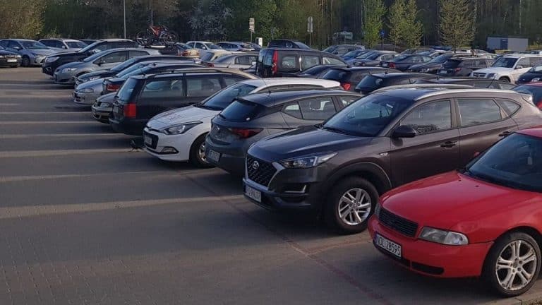 Parking lot pełen różnych samochodów, w tle drzewa i budynki.