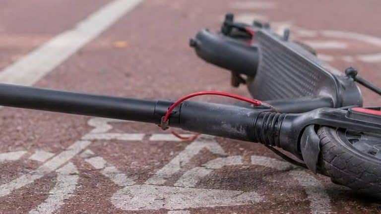 Zniszczona hulajnoga elektryczna leży na chodniku po wypadku.