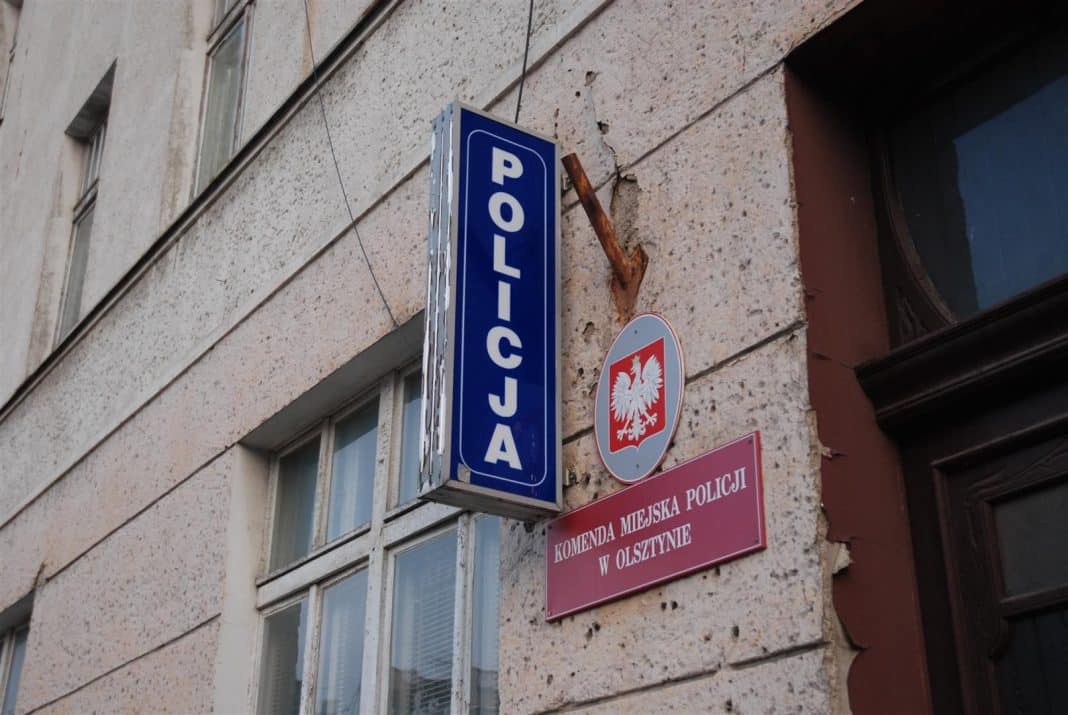 Zdjęcie budynku z oznakowaniem policji i herbem Polski na ścianie.