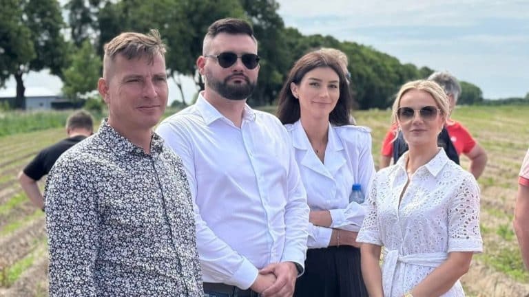 Grupa osób na polu podczas wydarzenia rolniczego, w tle drzewa i niebo.