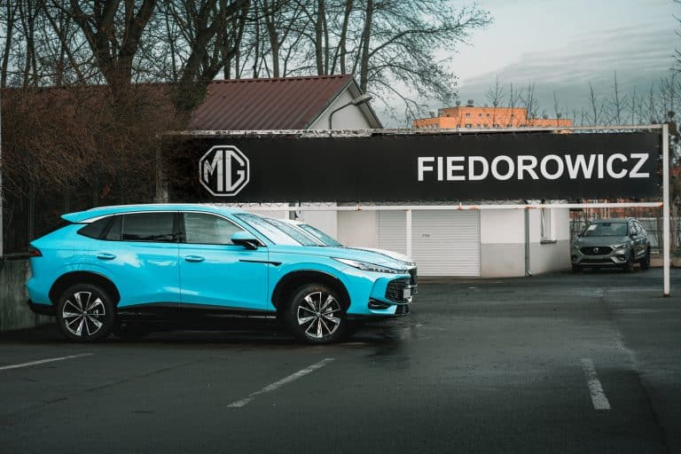Niebieski SUV zaparkowany przed salonem samochodowym MG w Olsztynie, widoczny napis FIEDOROWICZ na banerze.