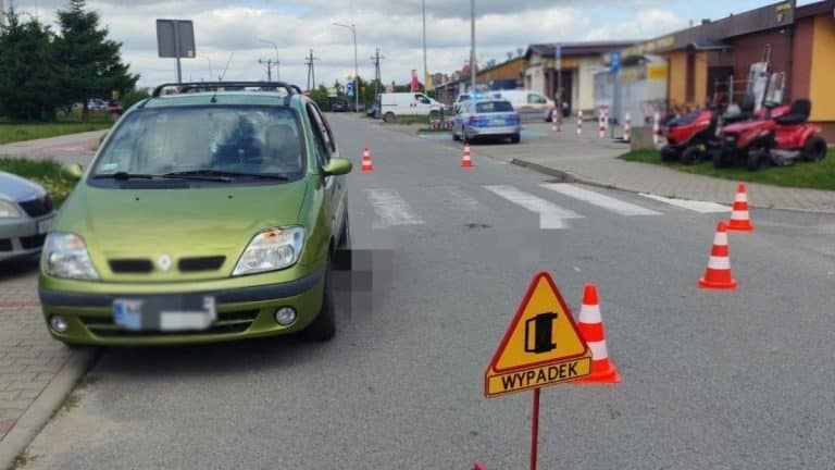 Zabezpieczony samochód na miejscu wypadku na przejściu dla pieszych, oznakowany znak i korki w tle.