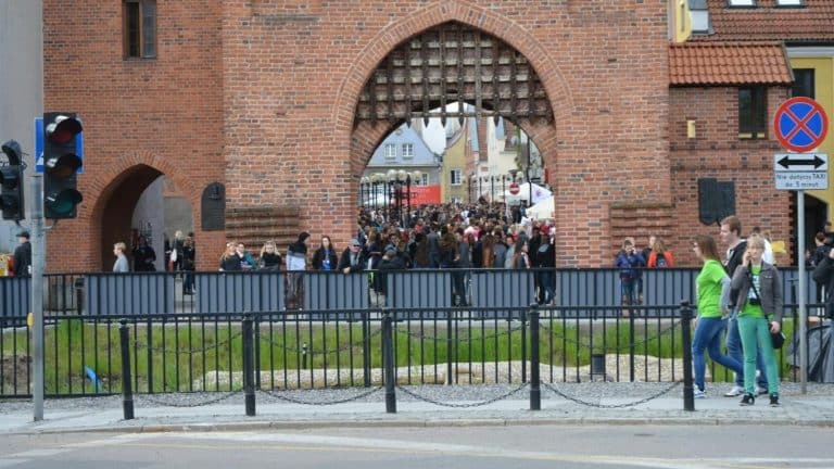 Widok na bramę wjazdową do zamku z dużym tłumem ludzi na dziedzińcu.