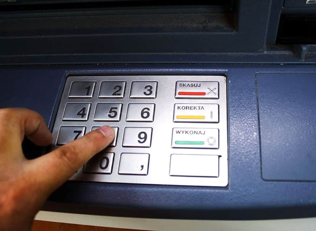 Zdjęcie bankomatu z klawiaturą i ręką w trakcie wpisywania kodu PIN.
