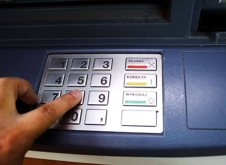 Zdjęcie bankomatu z klawiaturą i ręką w trakcie wpisywania kodu PIN.