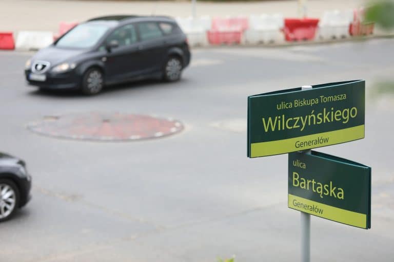 Tabliczki z nazwami ulic na skrzyżowaniu w Olsztynie, w tle ruch samochodów.