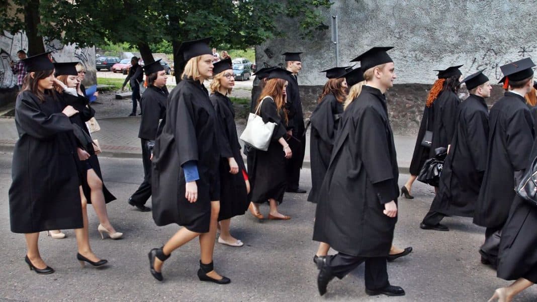 Grupa studentów w czarnych togach i czapkach podczas uroczystości ukończenia studiów na zewnątrz.