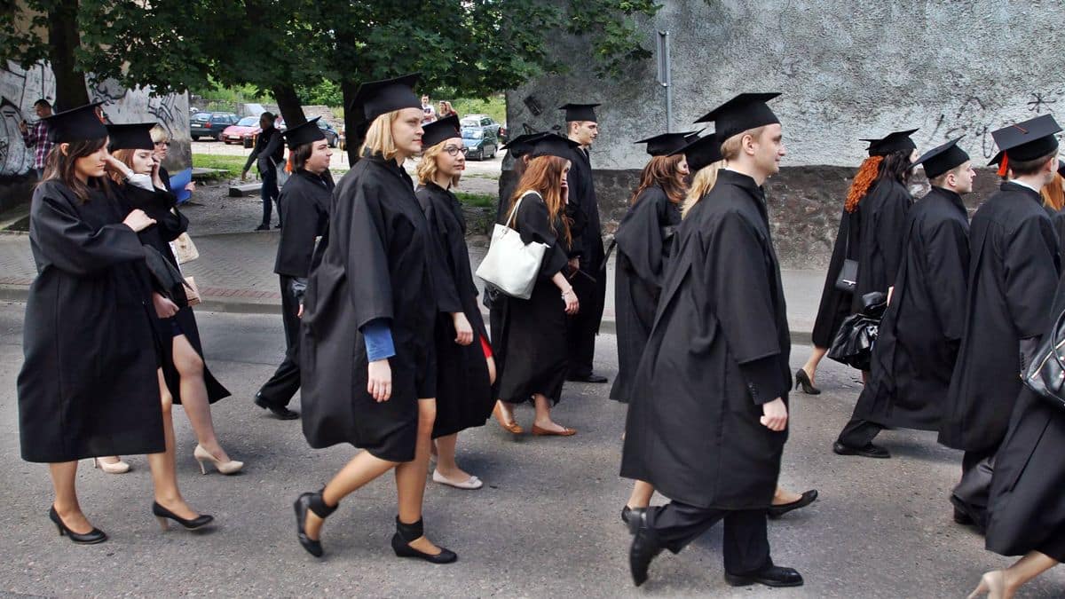 Grupa studentów w czarnych togach i czapkach podczas uroczystości ukończenia studiów na zewnątrz.