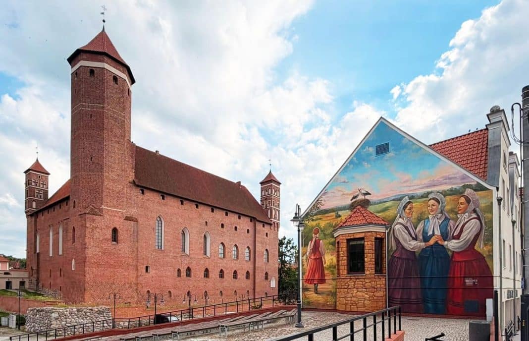 Mural przedstawiający tradycyjne postaci i krajobraz na ścianie budynku przy amfiteatrze w Lidzbarku Warmińskim, obok zamku.