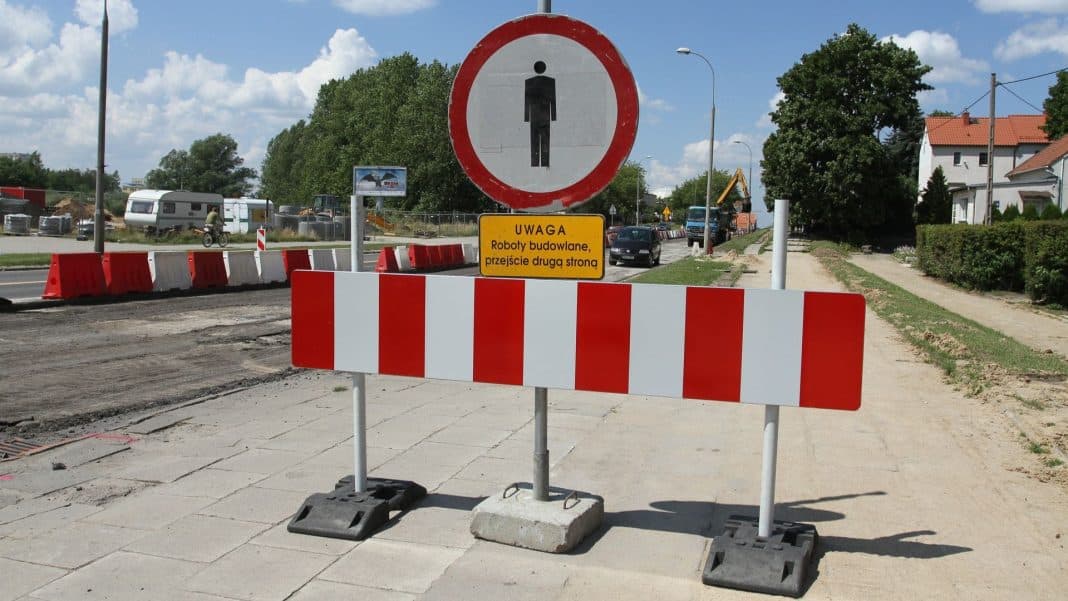 Zamknięte skrzyżowanie z oznakowaniem robot budowlanych i barierami na chodniku.