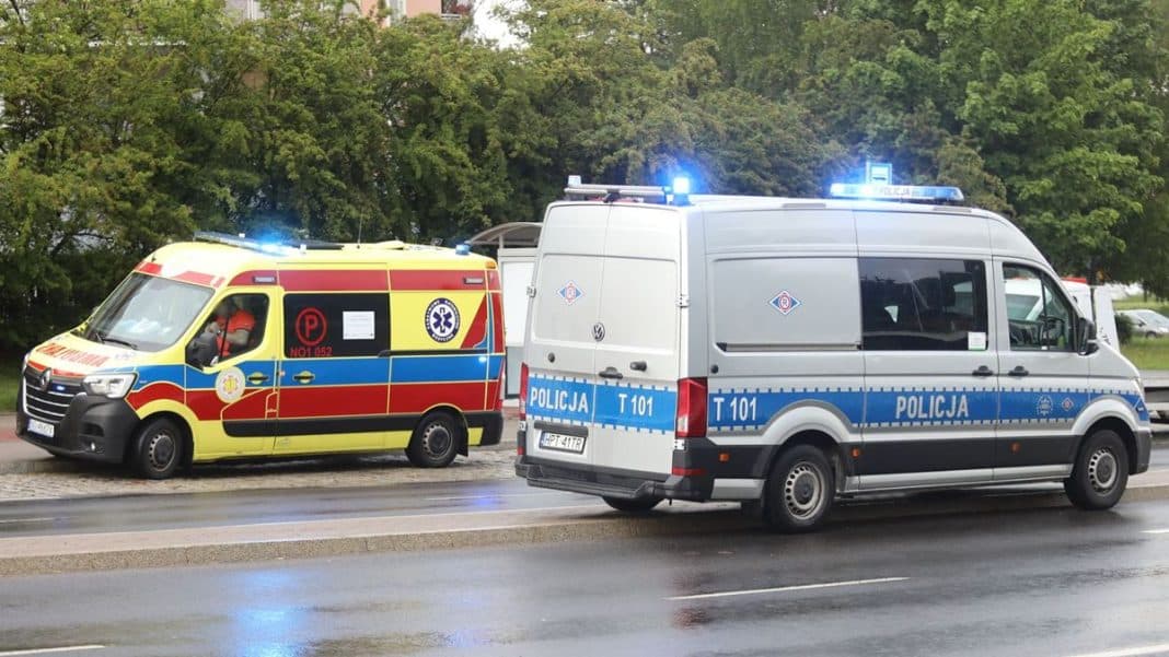 Na zdjęciu dwa oznakowane pojazdy policyjne i karetka na drodze w pobliżu zielonych drzew.