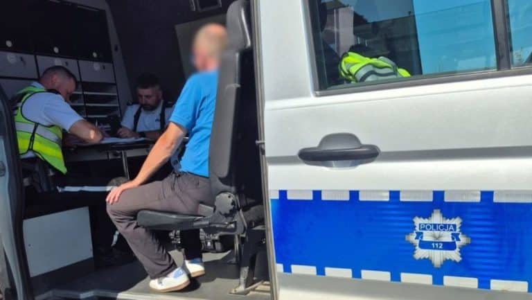 Kierowca autobusu siedzi na miejscu pasażera po badaniu alkomatem, w tle policjanci w biurze.