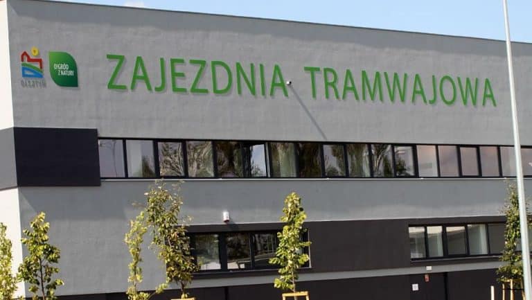 Budynek z napisem Zajezdnia Tramwajowa i logo Ogród z Natury na szarej ścianie.