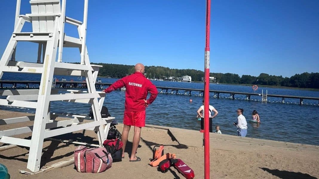 Ratownik nad jeziorem Ukiel, wokół leżaki i ludzie kąpiący się w wodzie.