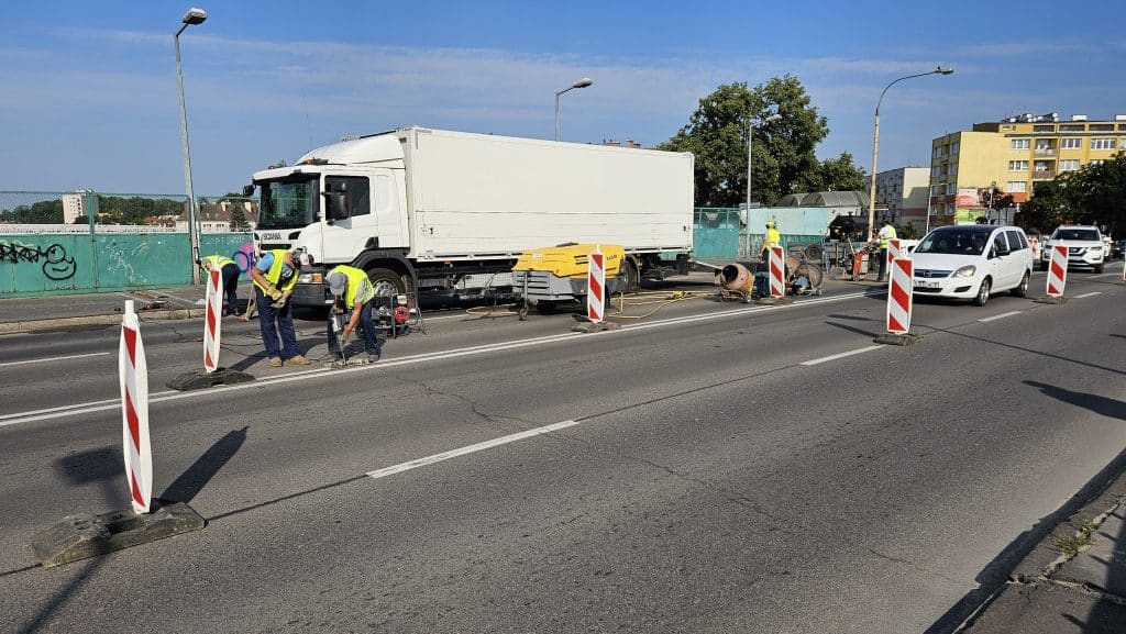 Prace remontowe na ul. Limanowskiego w Olsztynie, robotnicy pracują przy drodze, ustawione bariery i sprzęt budowlany.