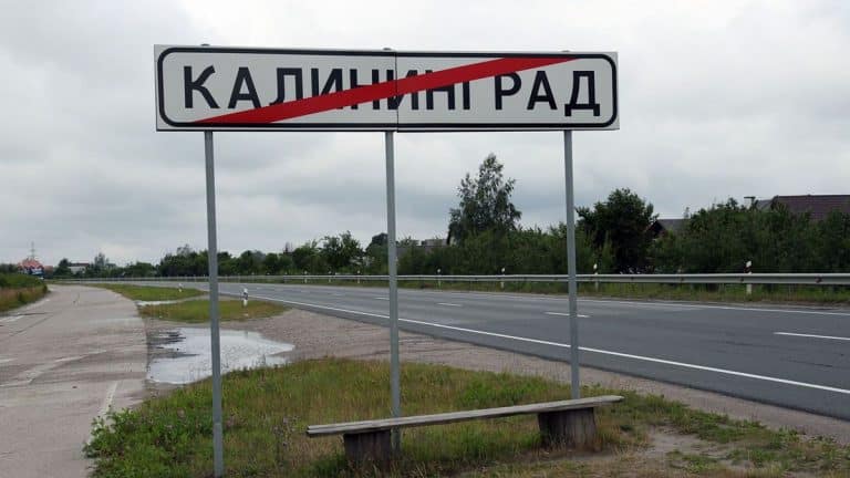 Tabliczka z nazwą miejscowości Kaliningrad przekreślona czerwoną kreską, obok droga i zielony krajobraz.