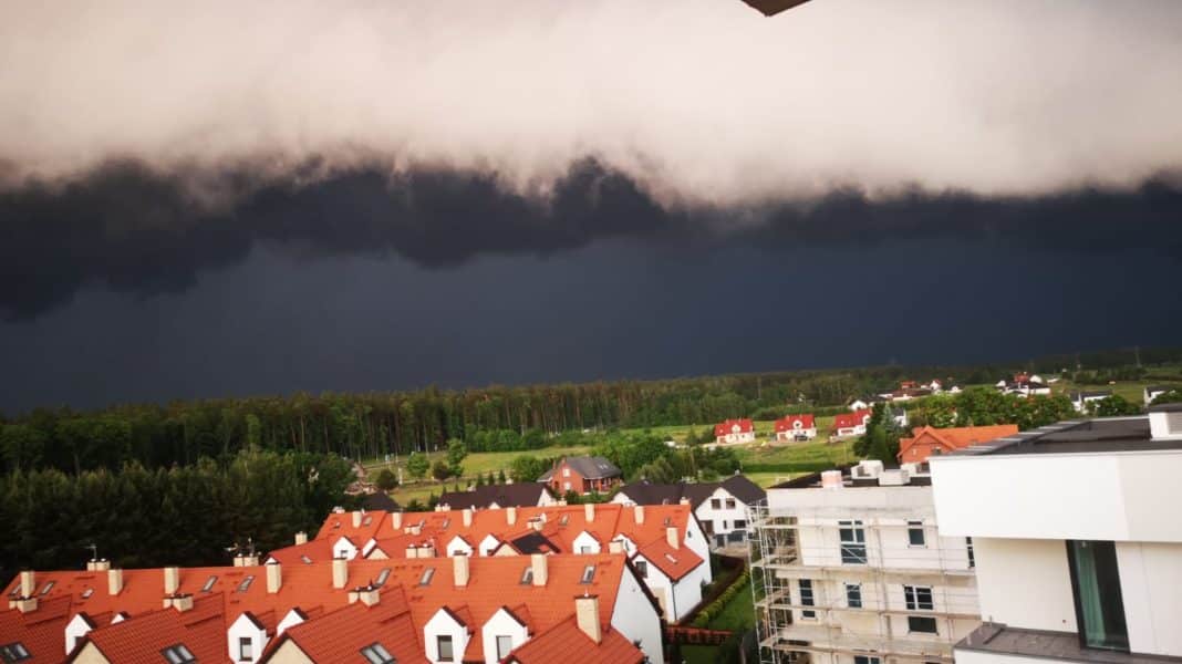 Ciemne, burzowe chmury nad miastem z czerwonymi dachami i zielonymi terenami w tle.