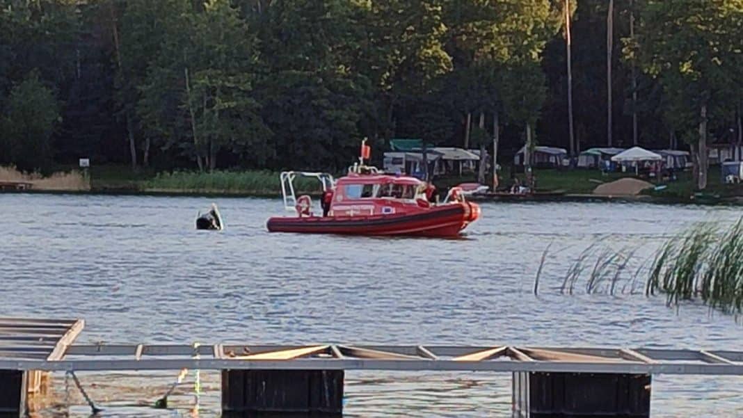 Czerwony ponton ratunkowy na jeziorze z widokiem na plażę i las w tle.
