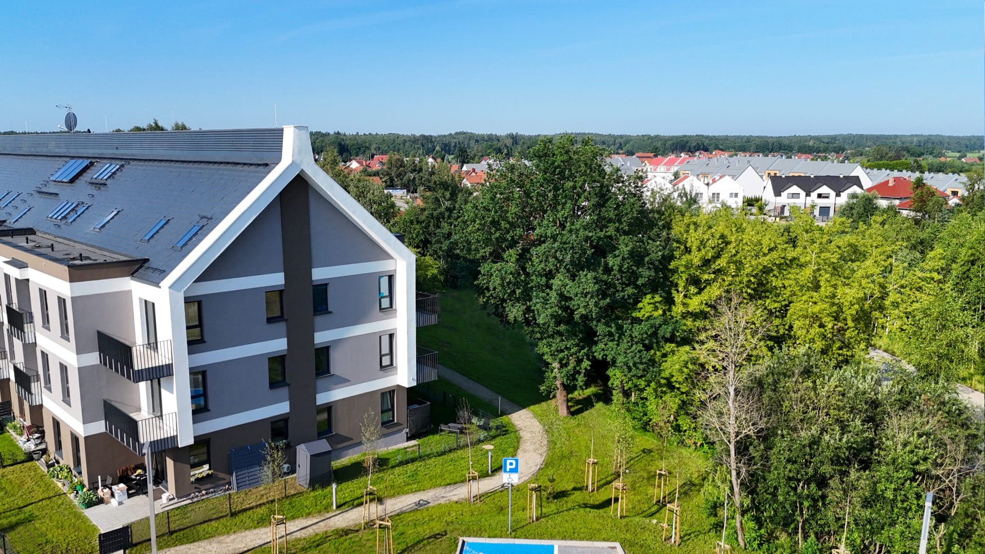 Widok na nowoczesny budynek mieszkalny w otoczeniu zieleni i innych domów w Gutkowie.