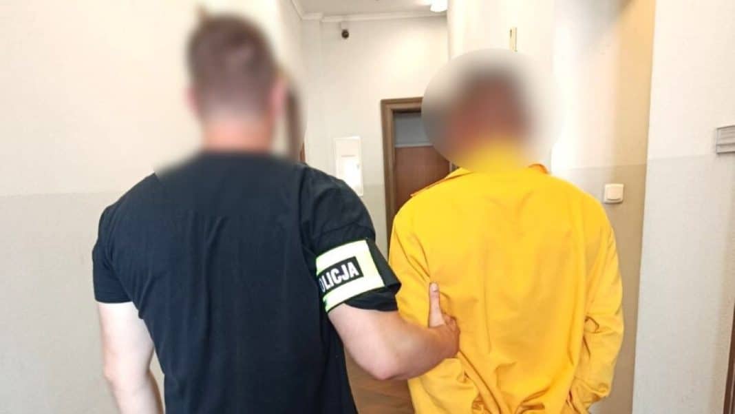 Policjant trzyma mężczyznę w żółtej kurtce podczas interwencji w mieszkaniu.