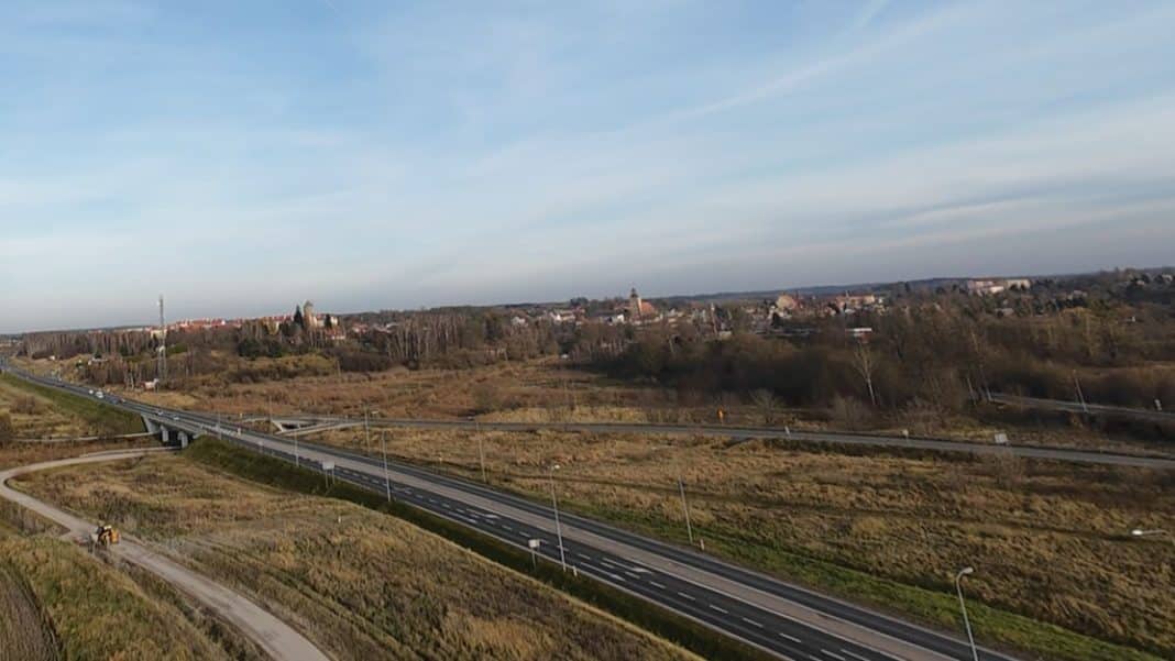 Widok na rozbudowaną drogę ekspresową S16 w okolicy Olsztyna, z nowymi pasami i infrastrukturą, na tle krajobrazu.