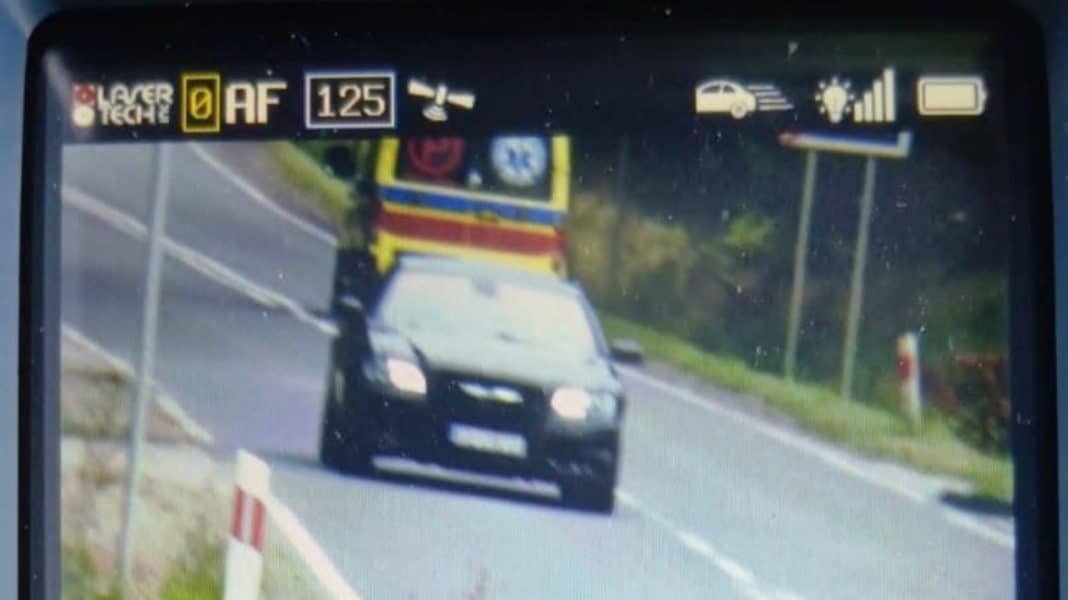 Zdjęcie z rejestratora prędkości pokazujące czarny samochód jadący po drodze w terenie zabudowanym.