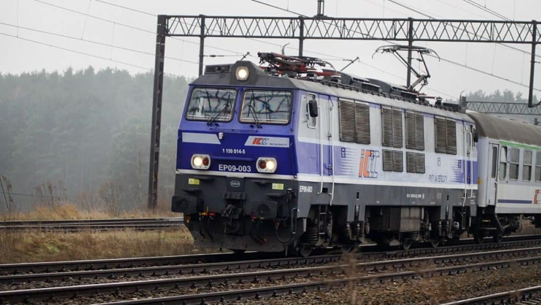 Lokomotywa elektryczna na torach, w tle linie trakcyjne i las.