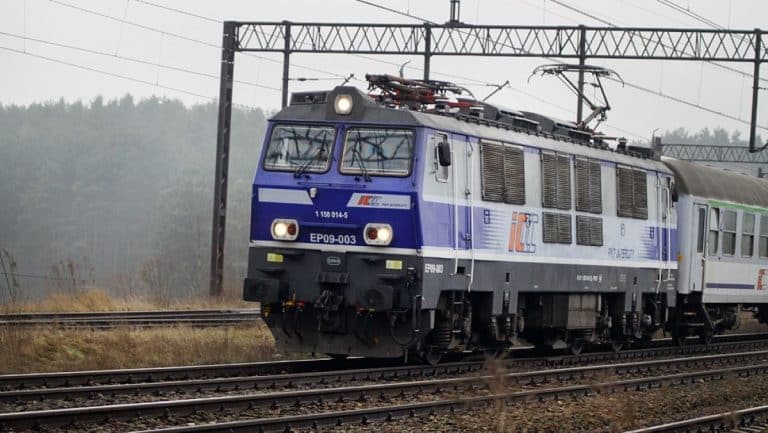 Lokomotywa elektryczna na torach, w tle linie trakcyjne i las.