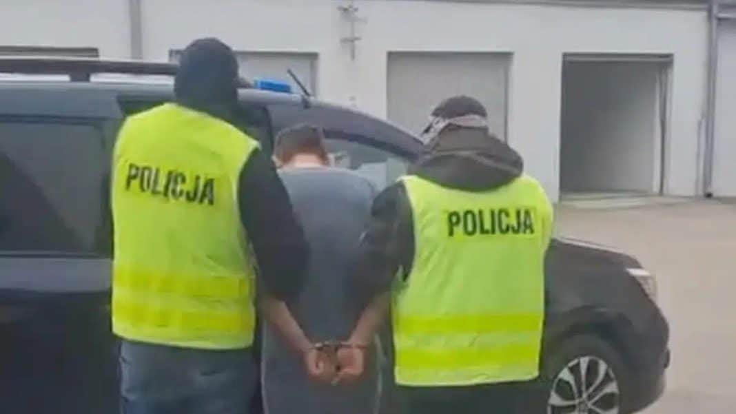 Mężczyzna w rękach policjantów, z tyłu radiowóz, na tle budynku.