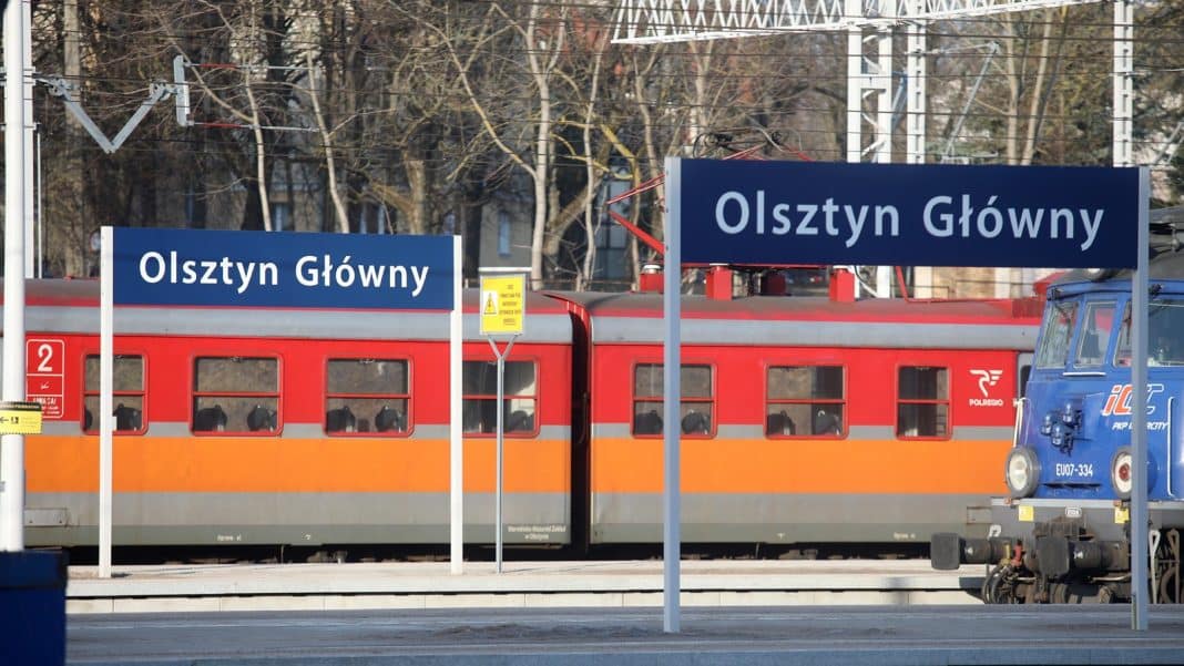 Pociąg regionalny na stacji Olsztyn Główny, widoczny jest peron i tablice z nazwą stacji.
