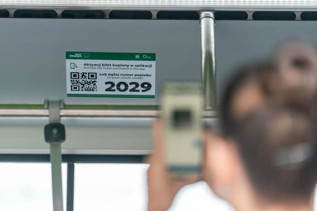 Na zdjęciu widoczny jest kod QR umieszczony w autobusie miejskim w Olsztynie, obok znajduje się informacja o konieczności wpisania numeru pojazdu.