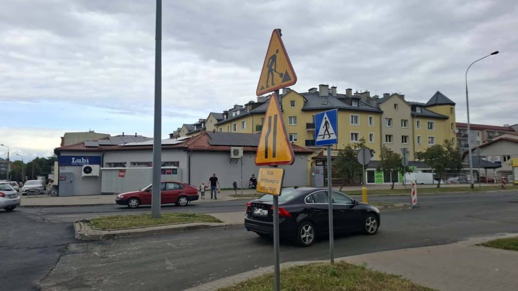 Znaki drogowe i zamknięte wjazdy na skrzyżowaniu w Olsztynie, w tle budynki mieszkalne i sklep.