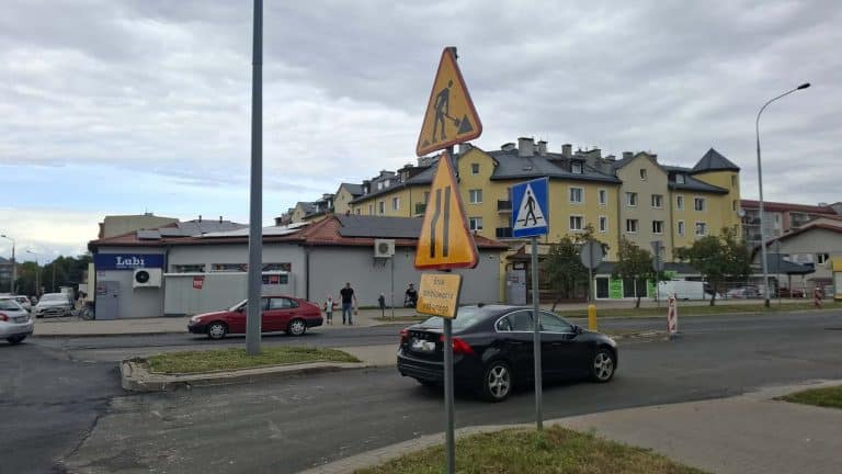 Znaki drogowe i zamknięte wjazdy na skrzyżowaniu w Olsztynie, w tle budynki mieszkalne i sklep.