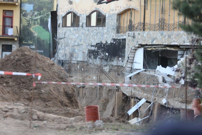 Uszkodzona zewnętrzna ściana hotelu podczas prac budowlanych, widoczny wyburzony fragment i zbrojenie.