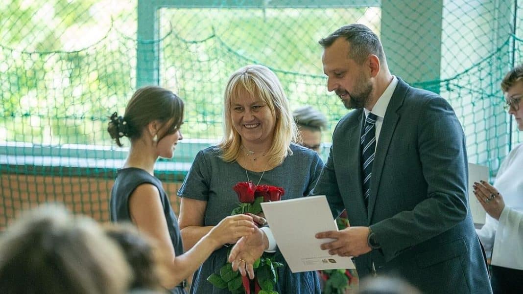 Nauczycielka otrzymuje od mężczyzny dyplom i kwiaty podczas uroczystości rozpoczęcia roku szkolnego w Olsztynie.