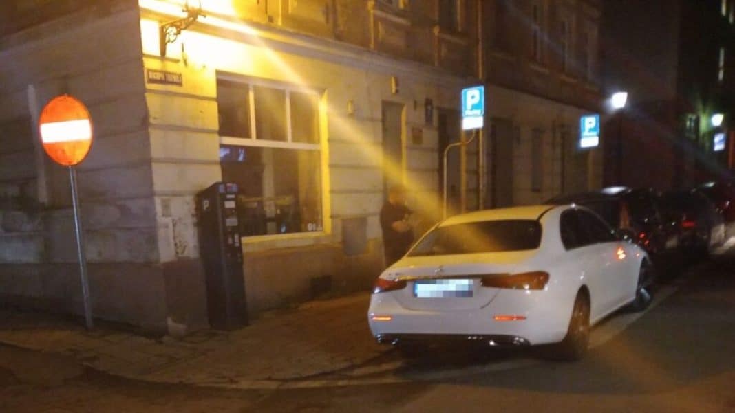 Nocna interwencja strażników przy białym Mercedesie na ulicy w Olsztynie, mężczyzna przy samochodzie.