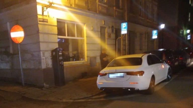 Nocna interwencja strażników przy białym Mercedesie na ulicy w Olsztynie, mężczyzna przy samochodzie.