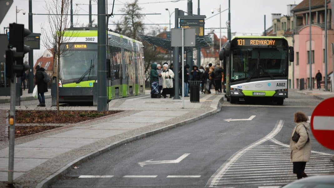 Autobusy i tramwaje na przystanku w Olsztynie z widocznymi naklejkami z kodami QR.