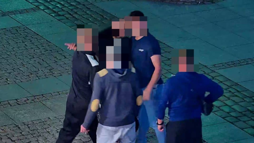 Grupa mężczyzn uczestnicząca w bójce na ulicy Starego Miasta, z widocznym monitorowaniem zdarzenia.