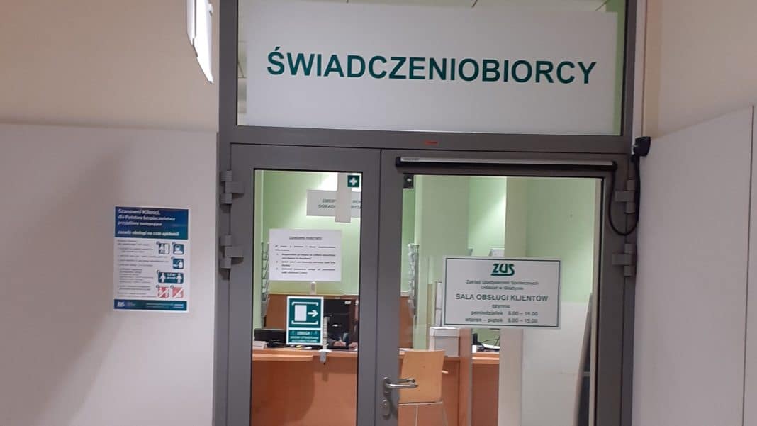 Widok na wejście do sali obsługi klienta ZUS z napisem 'Świadczeniobiorcy' nad drzwiami.