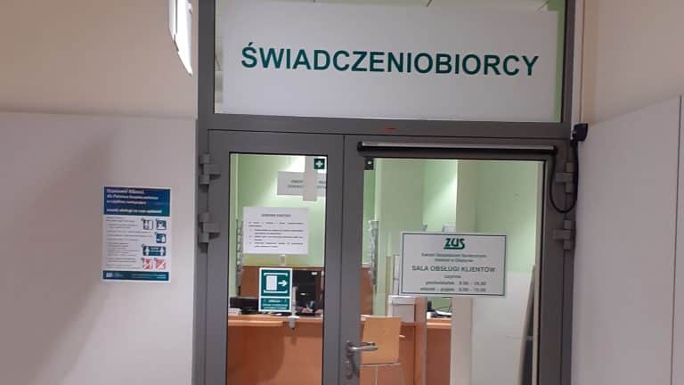 Widok na wejście do sali obsługi klienta ZUS z napisem 'Świadczeniobiorcy' nad drzwiami.