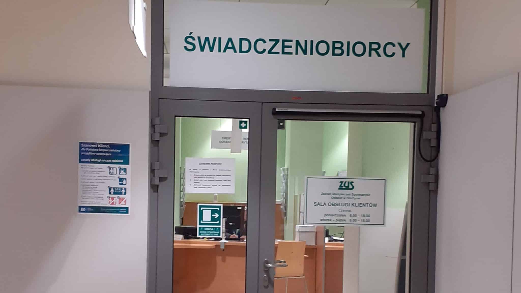 Widok na wejście do sali obsługi klienta ZUS z napisem 'Świadczeniobiorcy' nad drzwiami.